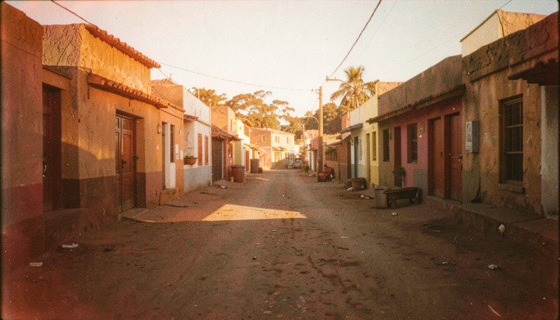 Warm-toned film still of a quiet street scene in an East African town, late-afternoon light casting long shadows, visible film grain