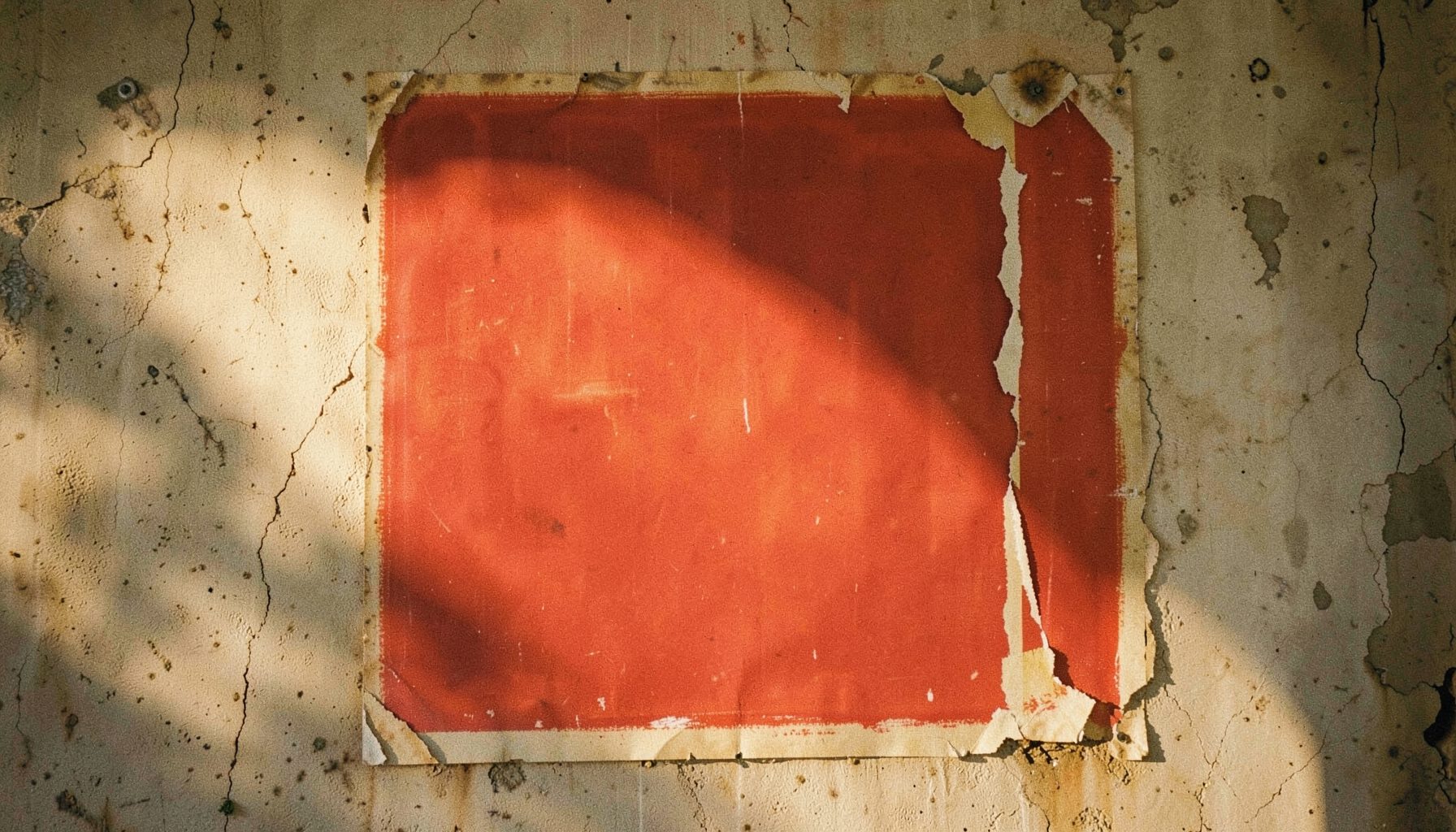 Hand-painted movie poster on a weathered wall, bold red and ochre colors, peeling edges, late-afternoon sunlight raking across the surface