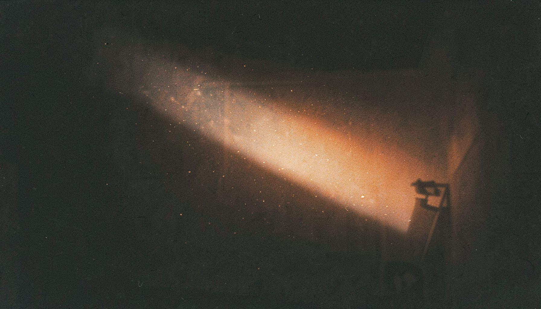 Projection light beam cutting through a dark room, dust particles visible in the shaft of light, moody and cinematic with visible grain