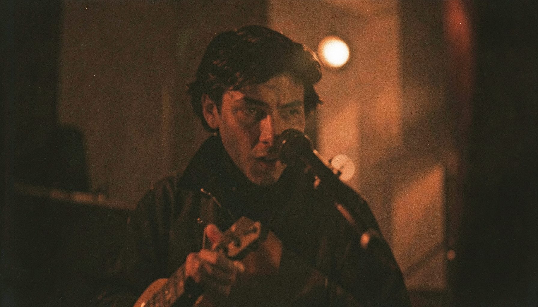 A soft-focus film portrait of a musician in a dim room, lit by a single warm tungsten source, with rich brown and charcoal shadows, evoking intimacy and artistry.