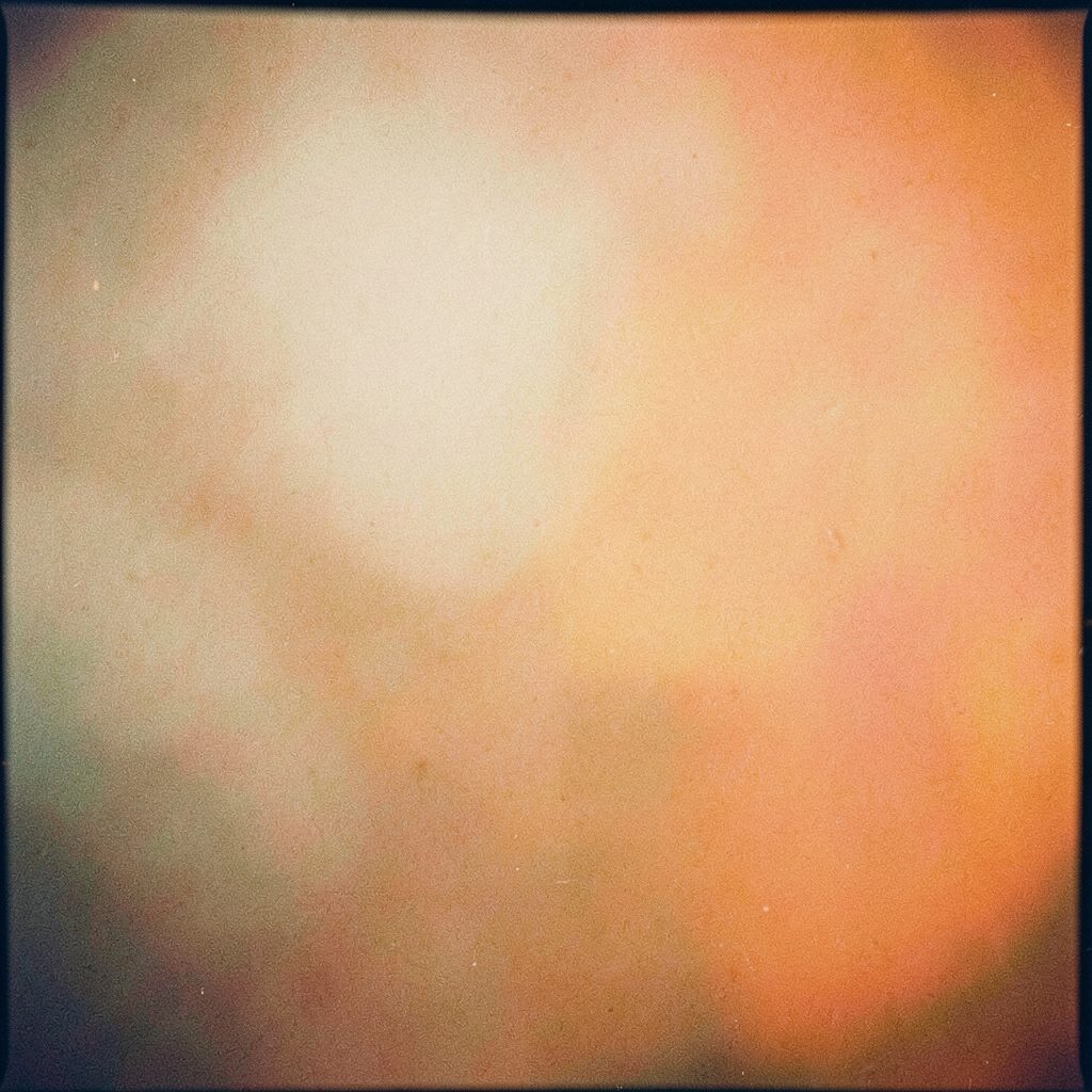 Grainy analog film photograph of a stage with warm amber and green stage lights, a hazy crowd silhouette, moody and energetic atmosphere